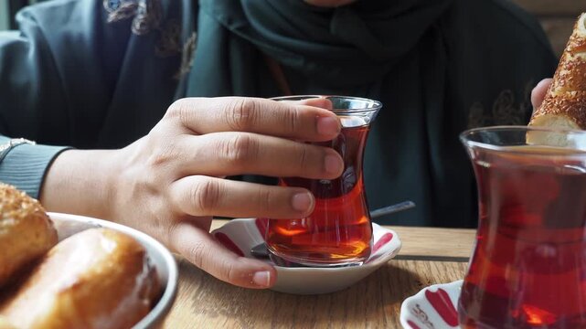 Woman wearing hijab drinking traditional turkish tea with sesame bagel in cafe environment close up shot