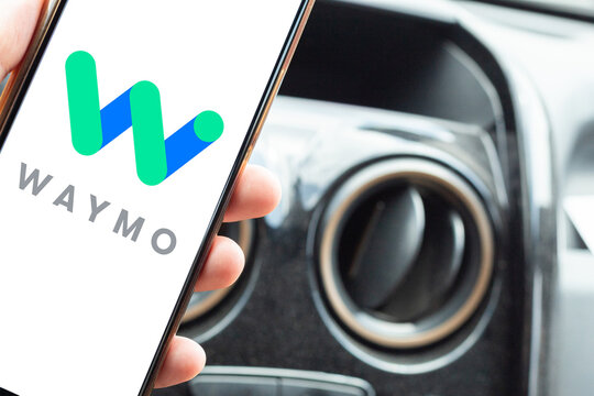 Passenger holding a cell phone with the Waymo logo inside the car. Concept of transportation technology and autonomous driving in a real-world context