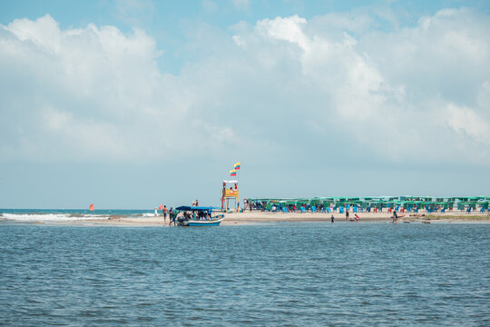 Buritaca beach in colombia presenting a lively public scene with a longboat arriving, people enjoying the sand, and rows of blue chairs under green umbrellas