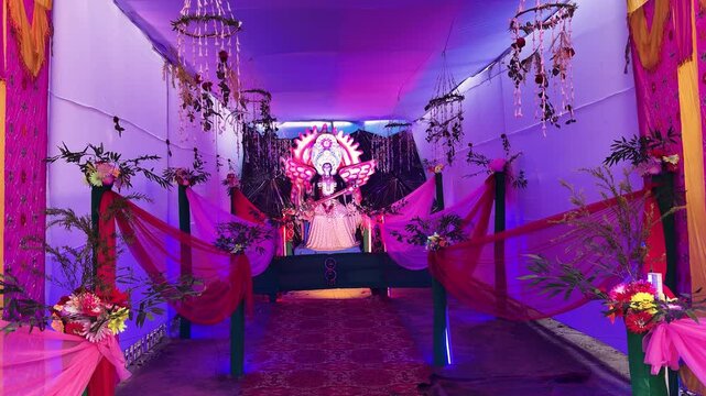 illuminated saraswati idol displayed in decorative indoor festival pandal with hanging flowers
