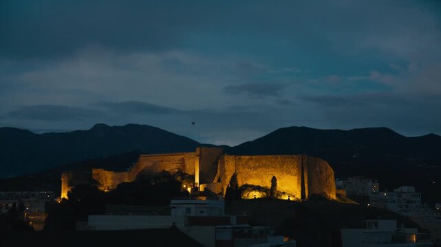 The historic fortress of Almu&ntilde;&eacute;car glowing at night against dark mountains and a deep blue evening sky in southern Spain.