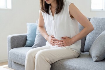 Obraz premium Young woman sitting on couch holding her stomach in pain