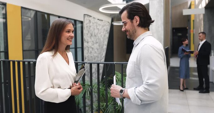Two colleagues standing in corporate office hallway, leading work-related conversation, discussing task or new project details, handshaking, finalizing talk, express mutual respect. Business relations