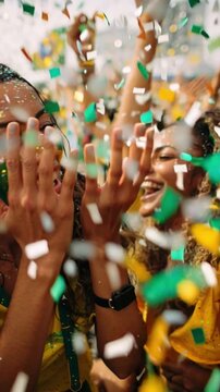 Group of happy Brazilian football fans with green and yellow face paint hugging and laughing under falling confetti