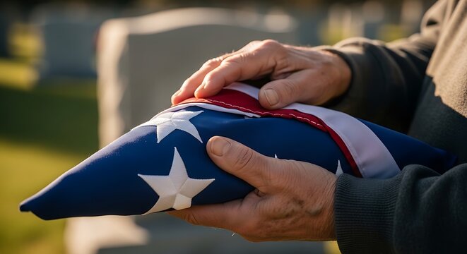 Person holding folded American flag at cemetery.