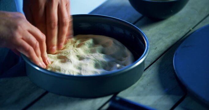 Cook's hands padding down pizza dough in pan - close up, high shot