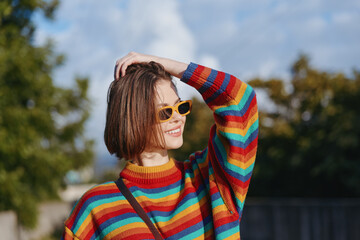 Woman portrait in a colorful rainbow sweater and yellow sunglasses smiling outdoors, casual fashion...