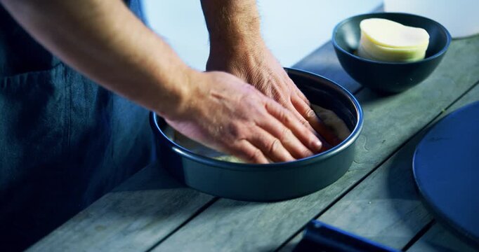 Hands of chef padding down pizza dough in tray - high, closeup shot