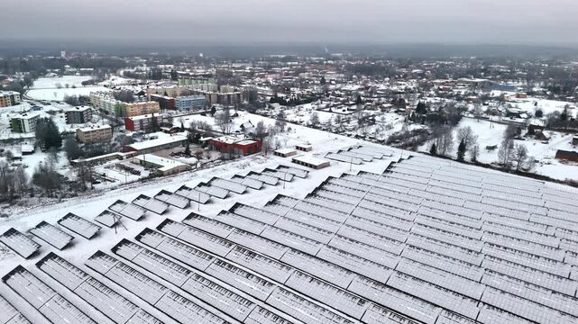 Bird's eye view of a snow covered field with solar panels next to a city.
