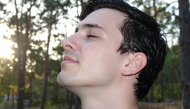 Joven adulto masculino con ojos cerrados disfrutando del aire fresco del bosque al atardecer.
