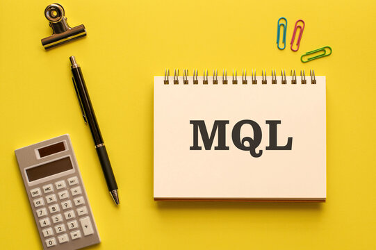 Eye-catching image of MQL text on notebook. The word stands for Marketing Qualified Lead. Shown with calculator, pen, clips.