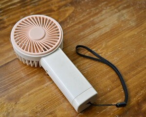 A white portable fan or handheld fan isolated on a wooden board. A handheld fan for traveling.