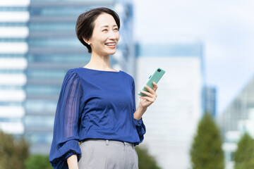 Fototapeta premium ビル街でスマートフォンを操作している女性