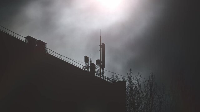 Bright Sunlight Highlights Rooftop Antenna Silhouette Featuring Parapet And Railings In Industrial Style