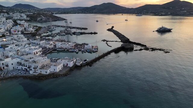 Paros Island,Aerial birds eye view,pan right from Naoussa town towards ancient Venetian castle's tower at harbor to the sunken sun behind the hills.Beautiful scenery with colorful sky.