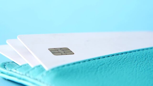 Three white plastic bank cards in teal leather wallet pocket on blue background