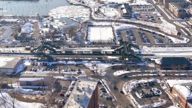 Aerial view of a snow covered perth amboy, new jersey, showing the train station, waterfront park, marina, and raritan bay with a commuter train arriving at the station