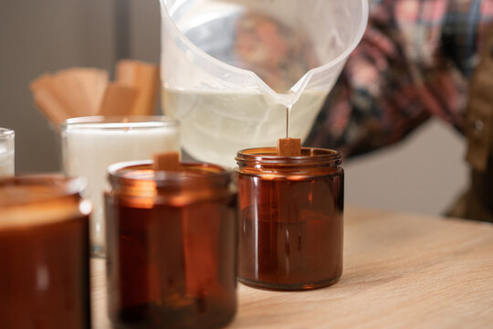 Concept of creative hobby and handmade candles. female hands pouring melted soy wax into jar.