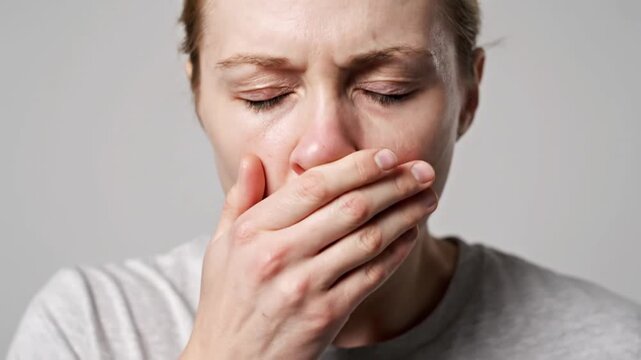 Professional realistic medium close shot of young adult sneezing into hand covering mouth natural reflex motion slight head forward movement pale face showing mild illness subtle redness around nose t
