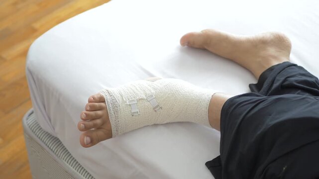 Injured male foot wrapped in white medical bandage lying on bed in hospital room cinematic steady shot