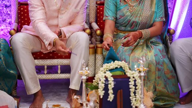 Indian or Pakistan couple seated in traditional attire during a wedding ceremony ritual. Close-up of hands performing cultural wedding customs with decorative elements and ceremonial setup.