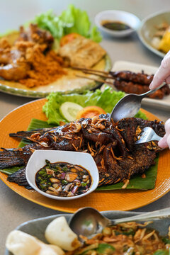 Person Using Spoon and Fork to Eat Sundanese Gurame Bakar Grilled Fish.