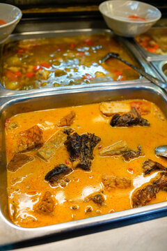 Traditional Indonesian mangut ikan, spicy coconut milk fish curry served in metal buffet tray. Authentic Southeast Asian cuisine with rich orange sauce and grilled fish pieces.