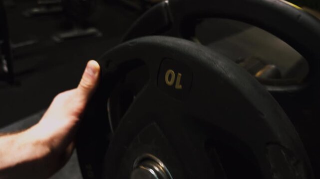 Close up of person placing 10 kilogram weight plate on gym machine. Strength training, fitness workout and muscle building concept.