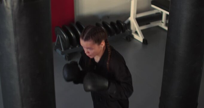 The teenage boxer powers through a punching bag session, blending agility, strength, and technique to elevate her boxing performance with every hit. Slow motion 4k footage.