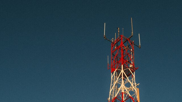 Red and White Communication Tower Against Clear Sky with People Below &ndash; Telecommunication Infrastructure Scene