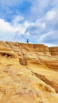 Person Standing on Golden Sandstone Cliffs Above the Ocean Under Dra