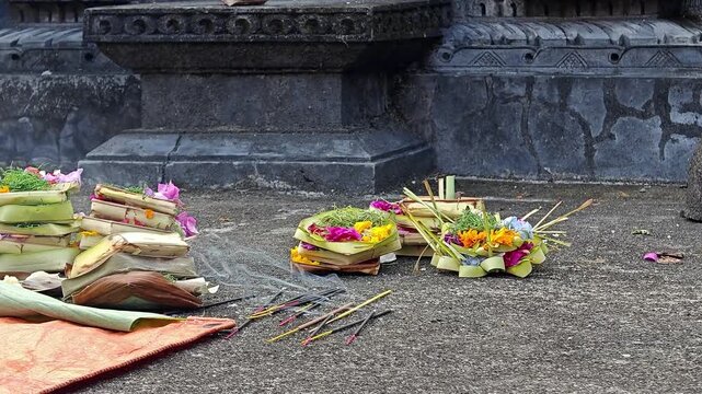Traditional Balinese Hindu Canang Sari Offerings with Burning Incense on Temple Ground
