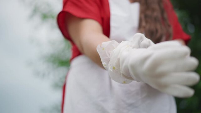 Mid shot white historical reenactor pulling delicate protective gloves over apron, textured fabric and careful handwork visible, slow methodical motion suggesting heritage craft and archival care