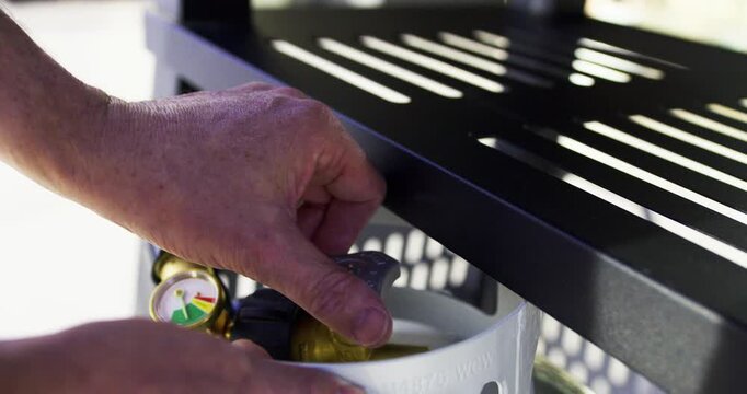 Man's hand twisting knob on propane tank then putting it under grill - closeup