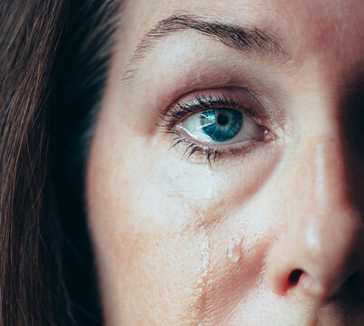 Close up of half of woman's eye with tears running down her cheeks.