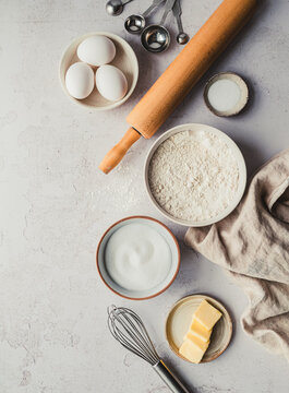 Top view of bowls of baking ingredients and tools on light background.