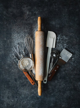 Overhead of flour dusted baking tools on black background.