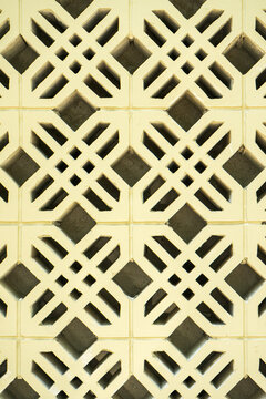 Close-up of a light yellow breezeblock wall with an intricate geometric cross pattern. This seamless architectural texture is perfect for modern abstract backgrounds and exterior design.