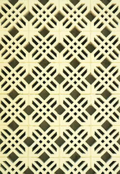 Close-up of a light yellow breezeblock wall with an intricate geometric cross pattern. This seamless architectural texture is perfect for modern abstract backgrounds and exterior design.