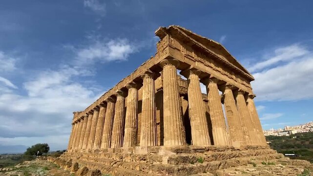 Cinematic left-to-right moving shot of the ancient Greek ruins in Agrigento, Sicily, showcasing the majestic Doric columns of the Valley of the Temples under a dramatic blue sky. The camera movement h