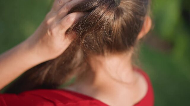 Caucasian woman ponytail red shirt outdoors sunlight highlights flakes on brunette strands, hand inspects scalp near nape, closeup backofhead shots capture texture and movement, candid selfcare