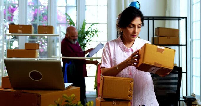 Indian senior couple doing E-commerce business from home, busy working in office managing online orders, packing parcels, dispatching boxes, taking customer calls and handling inventory together