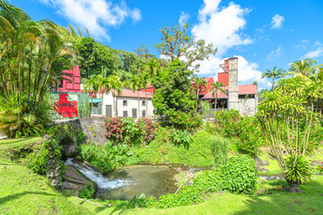 Fototapeta premium Martinique, French Antilles - Dec 27, 2025: Stream flowing through the tropical garden of Rhum JM distillery, surrounded by dense greenery and palm trees in Martinique