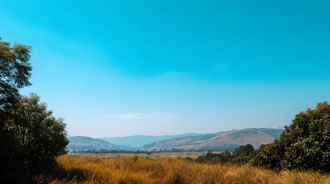 A vast serene landscape featuring rolling hills and golden grasslands beneath a clear bright blue sky