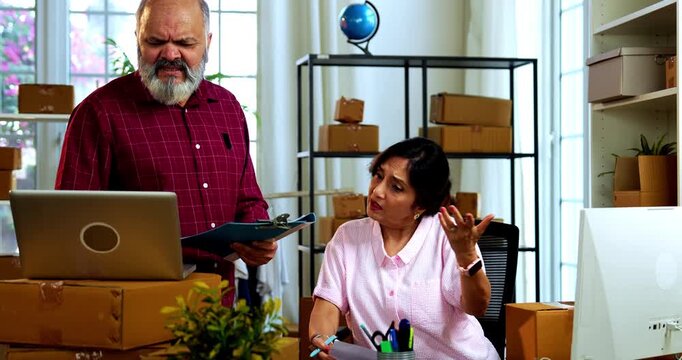 Indian senior couple showing stress doing E-commerce business from home while managing online orders, dispatching parcels, packing cardboard boxes and handling hectic workload in home office