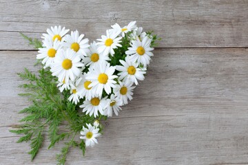 a heart shaped arrangement of daisies on a wooden background