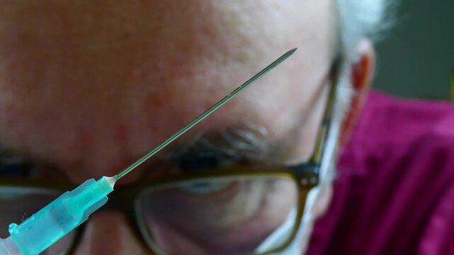 Senior man looking at hypodermic needle tip