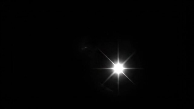 A dark night sky with bright starburst and small, distant blurred object