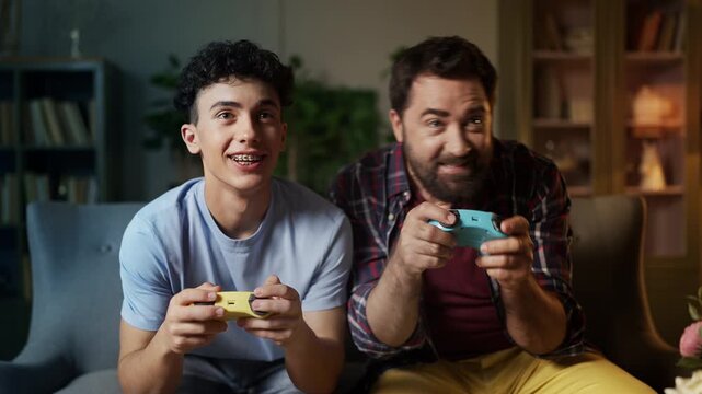 Cheerful middle-aged man and his teen son playing video game with gamepads
