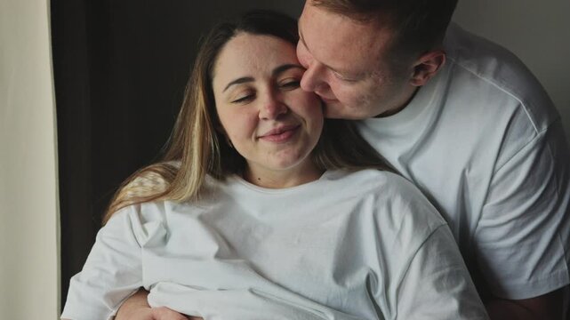 Pregnant woman and husband holding blue booties on belly. Happy expectant parents share tender moment at home. Concept for pregnancy announcement, parenthood, or family lifestyle content.